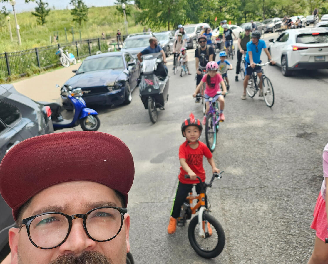 Untitled A selfie taken by a man on a bike with a growing column of kids on bikes in the background